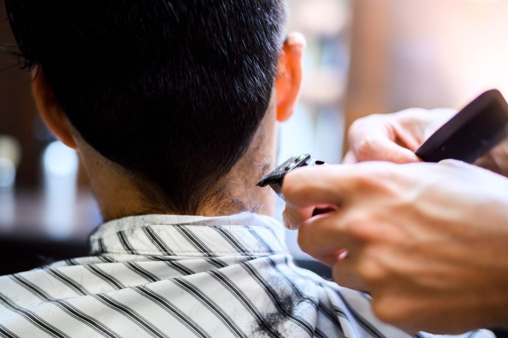 Expert barber trimming neckline at a walk-in barber shop, using clippers and comb in a cozy salon setting.