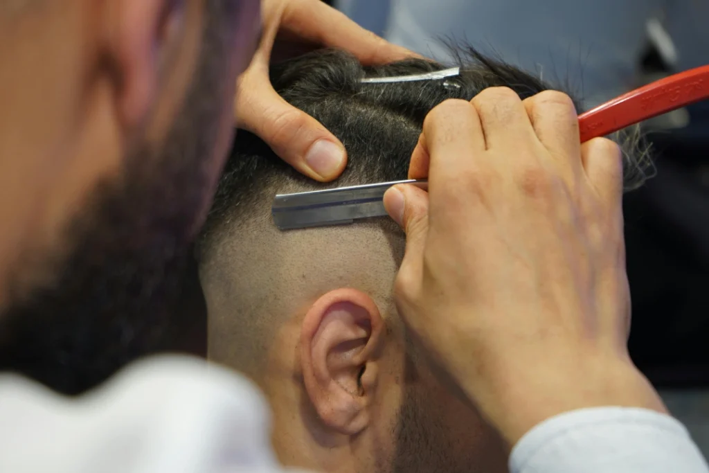 Barber carefully trimming the side and ear line with a detail clipper during a modern Mens haircut.