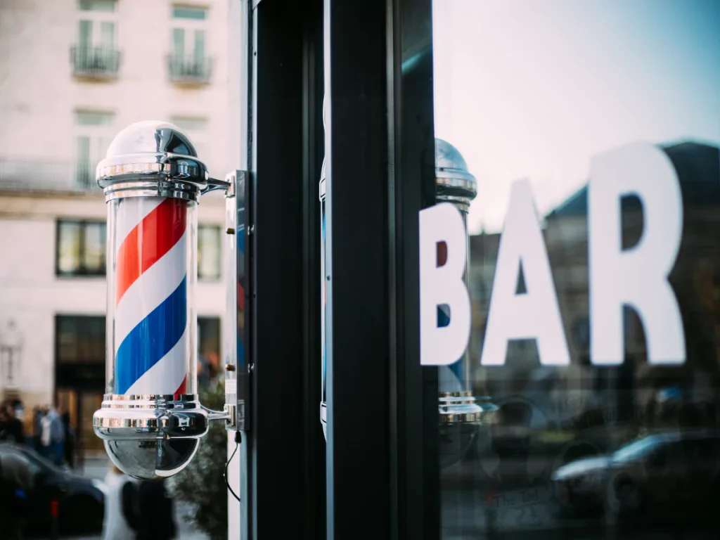 Classic barber pole outside Cheap Barber Shops storefront with 'BAR' sign on window