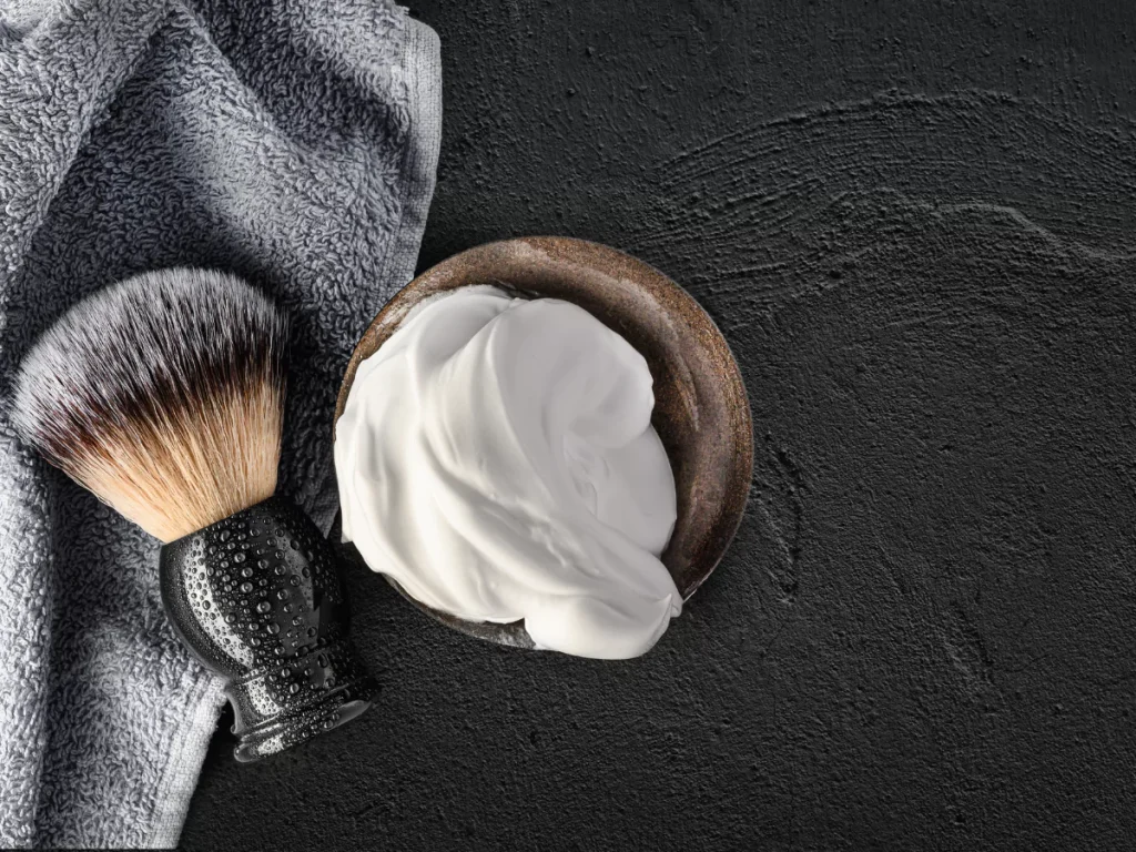 Close-up of a luxurious shave setup with a shaving brush and rich foam in a bowl, paired with a soft towel, ideal for a premium Haircut and Shave Houston experience.