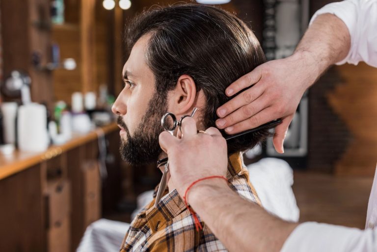 Barber trimming hair with scissors at a Houston barbershop, offering expert styling services.