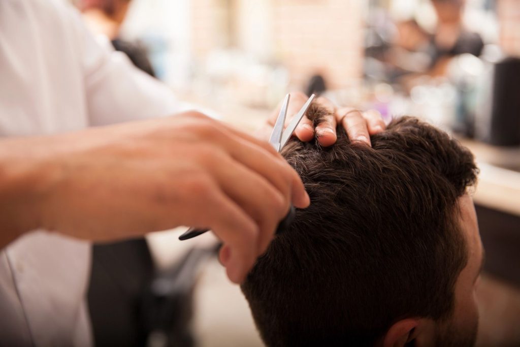 Barber trimming hair with scissors for a stylish men's haircut in a busy barbershop environment.