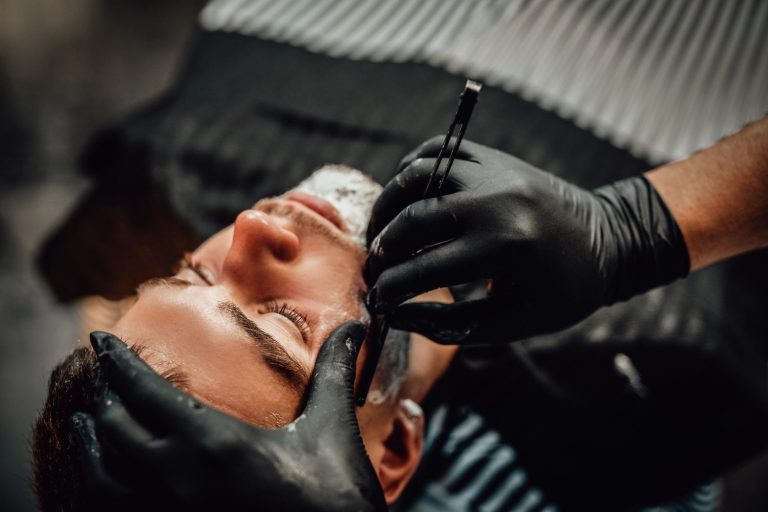 Barber giving a precise straight razor shave to client, enhancing a fresh men's haircut in barbershop setting.
