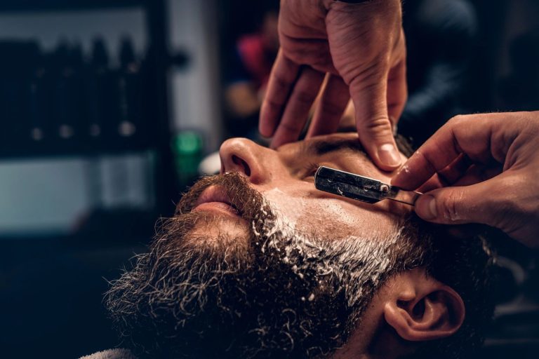Barber performing a clean men's shave at a Houston barbershop with a straight razor and hot towel.