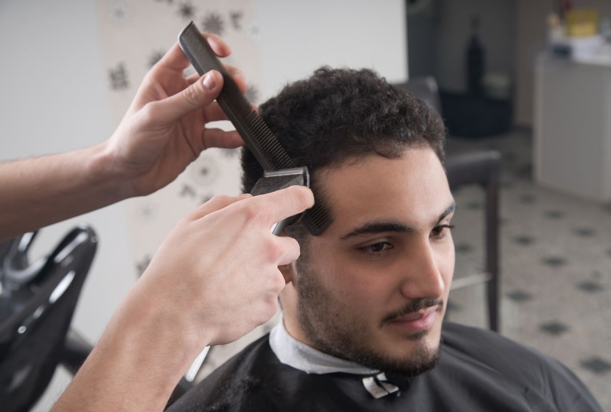 Barber shop Houston stylist trims curly hair with clippers and comb, delivering sharp fades and personalized service.