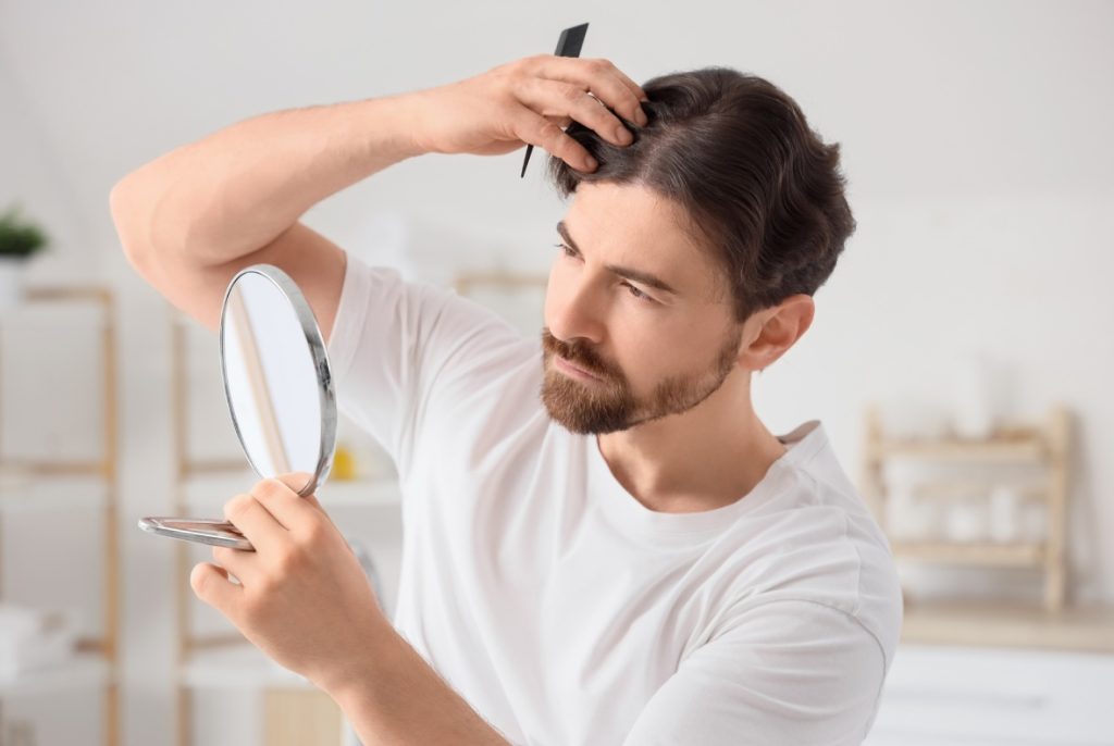 Man styling a fresh cut, checking mirror. Looks great after a visit to a quality Barber Shop.